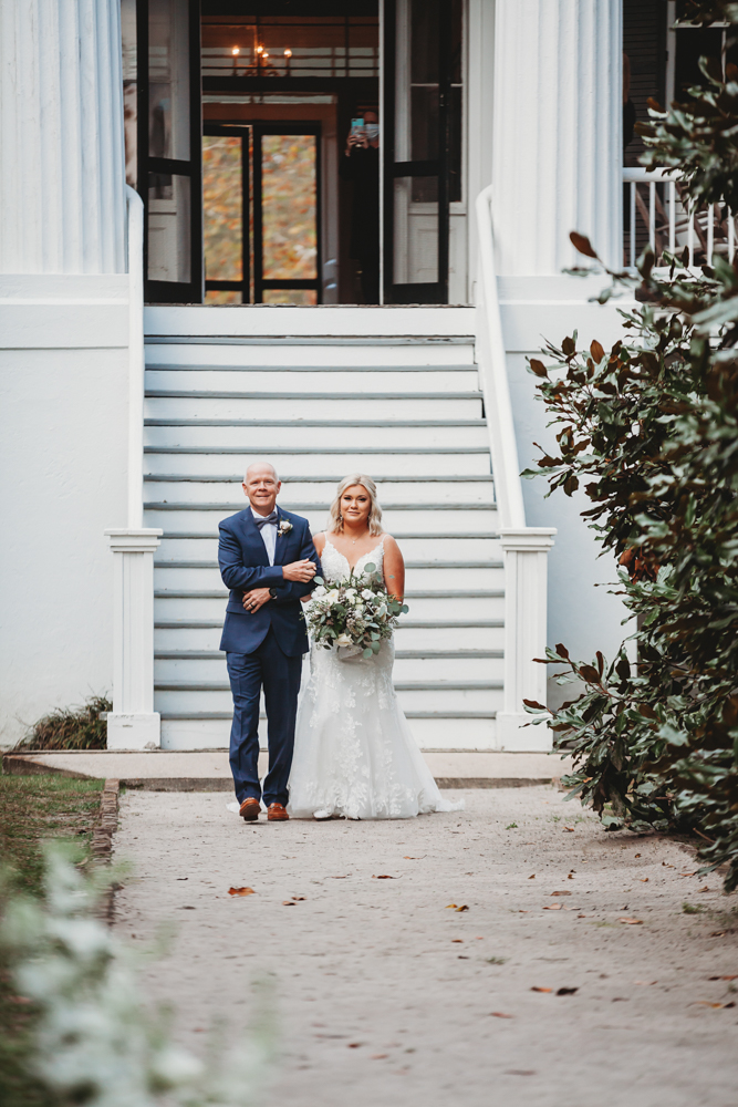 Bride Morgan walks down the steps with her father onto the aisle lined with greenery at Wavering Place.