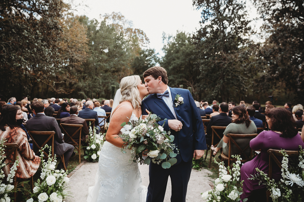 Recessional kiss as Morgan and Daniel walk back down the aisle with eucalyptus bouquet and smiling guests in the background at Wavering Place, Eastover SC