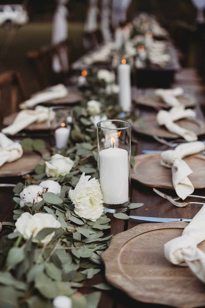 Close-up of reception table with wood chargers, cotton and eucalyptus runner, and glowing candlelight setting at Wavering Place in Eastover, SC