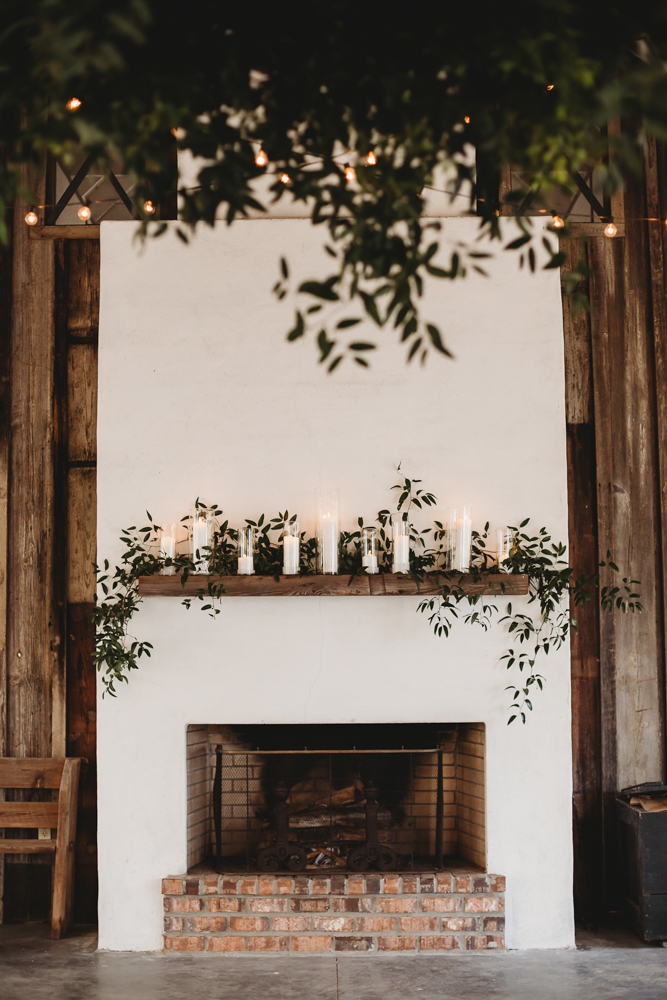 Large outdoor fireplace with candles and greenery on wooden mantel under hanging string lights at Wavering Place during Morgan and Daniel's reception
