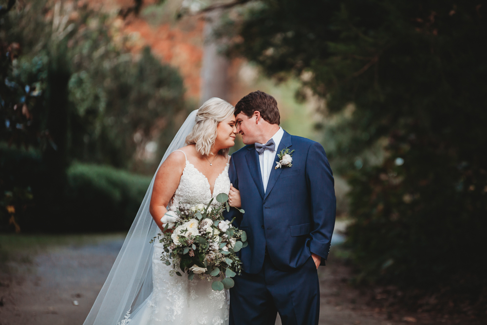 Tender moment on wooded path as Morgan and Daniel lean foreheads together, surrounded by nature at Wavering Place in Eastover SC