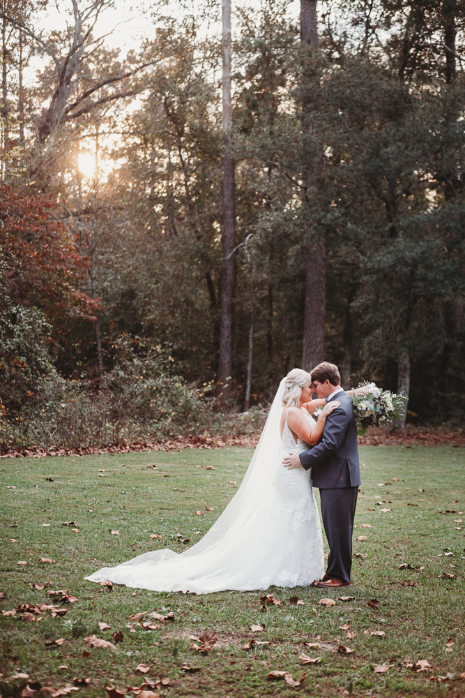 Golden hour embrace on a quiet lawn surrounded by trees as the sun sets behind Morgan and Daniel at Wavering Place in Eastover, SC