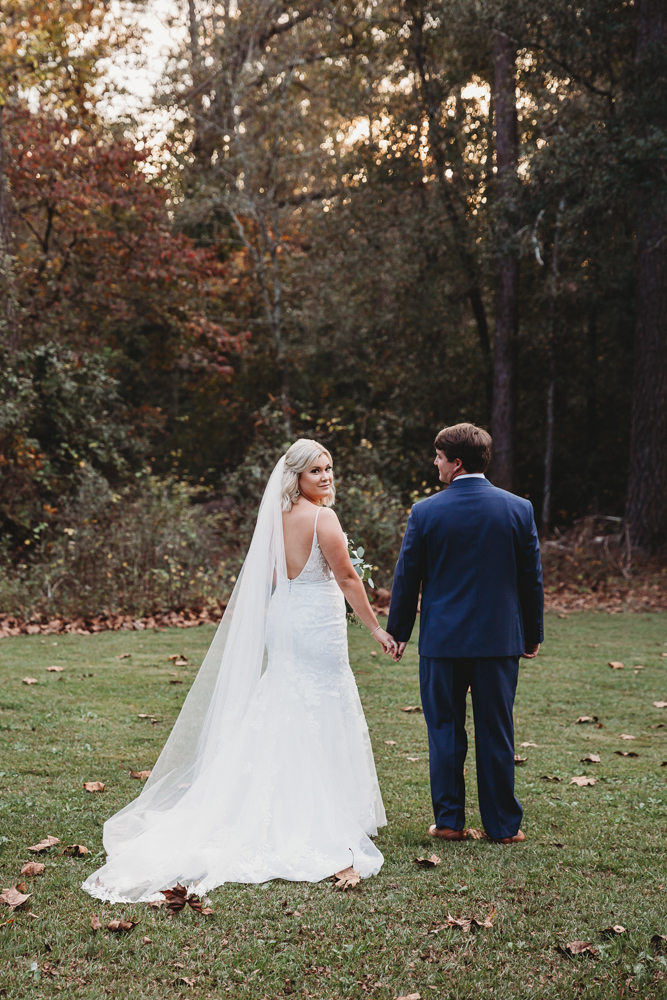Bride and groom walk away hand in hand with Morgan’s long veil trailing behind, captured in golden light at Wavering Place