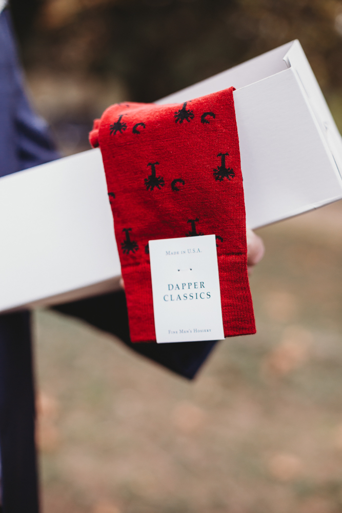 Close-up of red Dapper Classics socks with Palmetto and Crescent moon symbol, a fun groom detail from Morgan and Daniel’s wedding