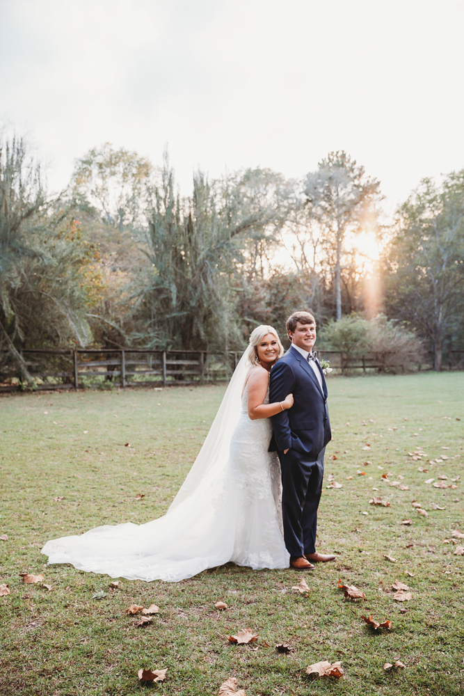 Morgan hugging Daniel from behind as they smile toward the camera, golden light casting a warm glow over the field at Wavering Place