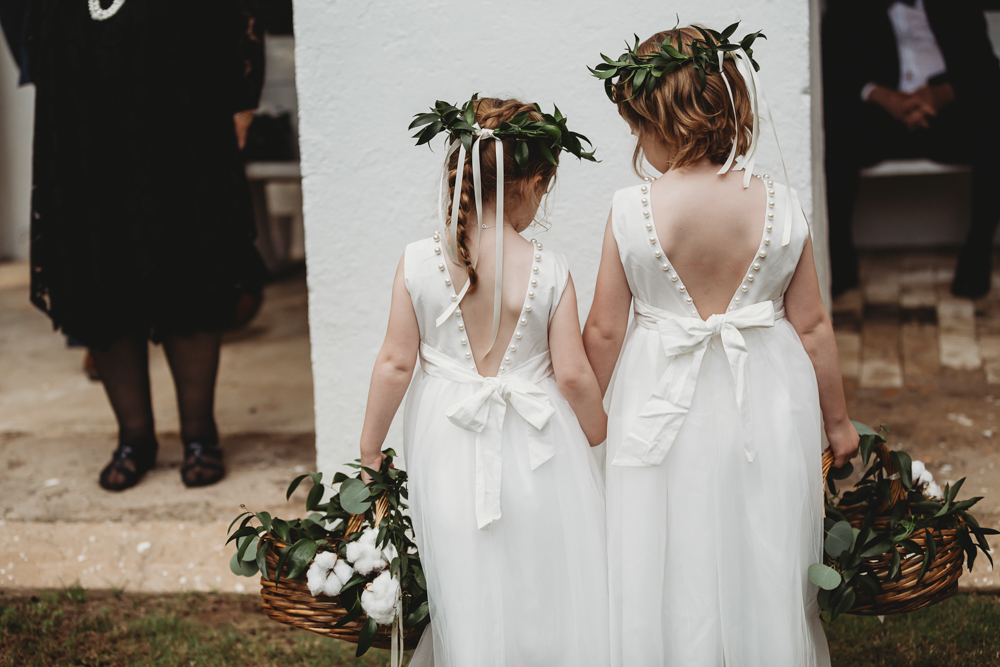 Back view of two flower girls in white dresses with pearl bows and cotton greenery baskets before the ceremony at Wavering Place