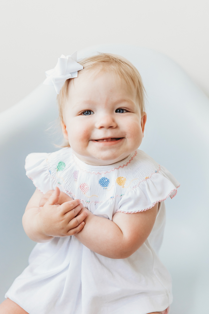 Close-up of Hadley's joyful expression in a smocked outfit, showing bright eyes and soft curls at Reflection Images