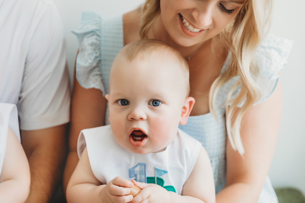 One twin cuddled in mom's arms, both smiling in studio at Reflection Images by Tracy Rowell in Florence SC