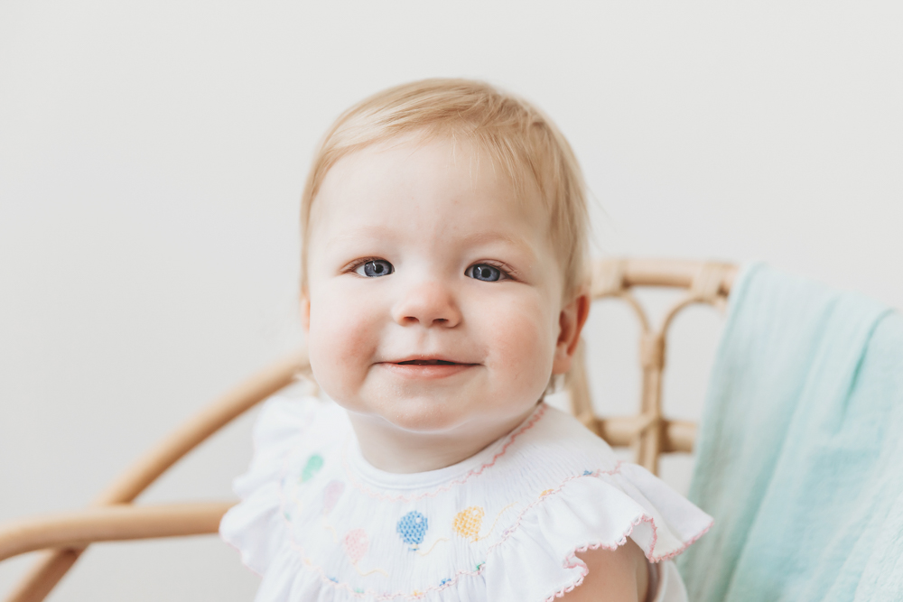 Close-up of Hadley's joyful expression in a smocked outfit, showing bright eyes and soft curls at Reflection Images