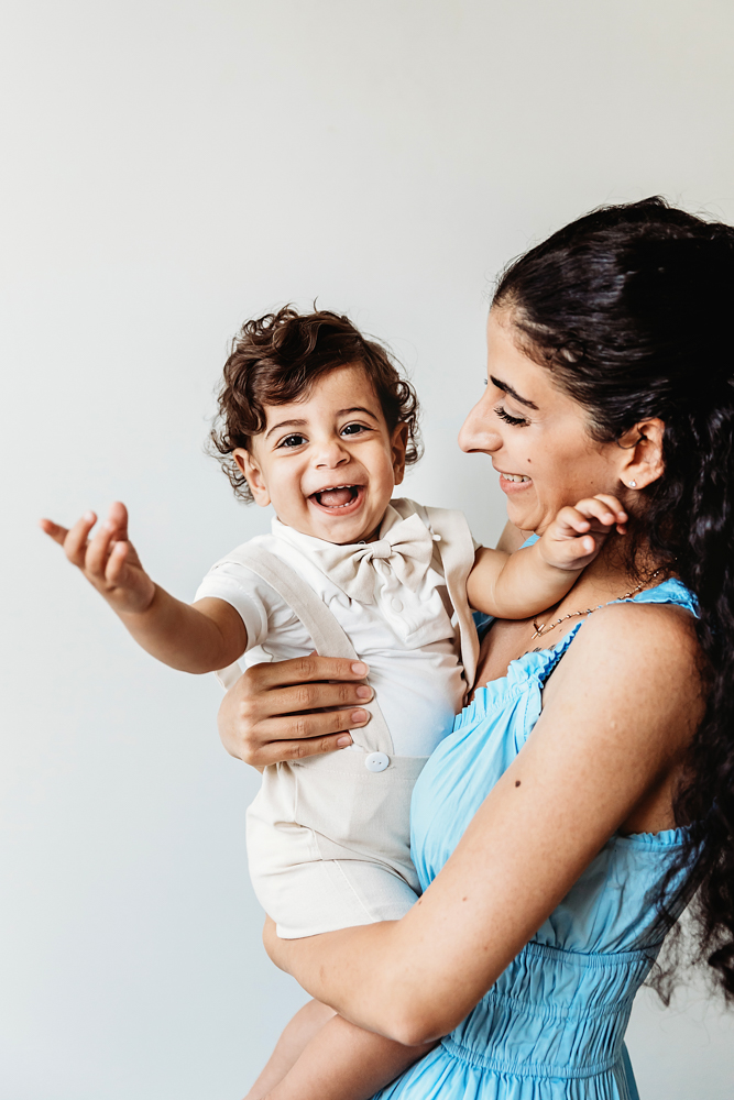 Lucas smiling and reaching forward while mom holds him against a clean white studio backdrop at Reflection Images by Tracy Rowell in Florence SC