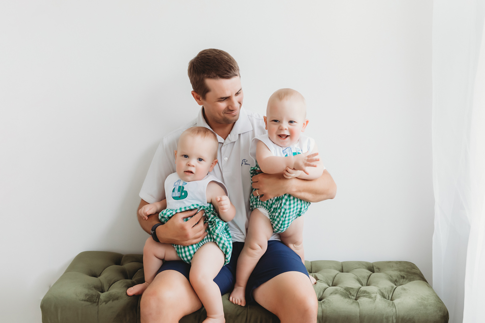 Dad smiling and holding both twins on green bench in studio at Reflection Images by Tracy Rowell in Florence SC