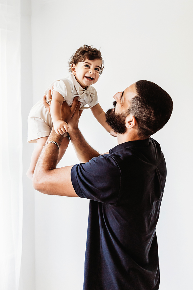 Dad lifting Lucas playfully toward the window light as he smiles brightly at Reflection Images by Tracy Rowell in Florence SC