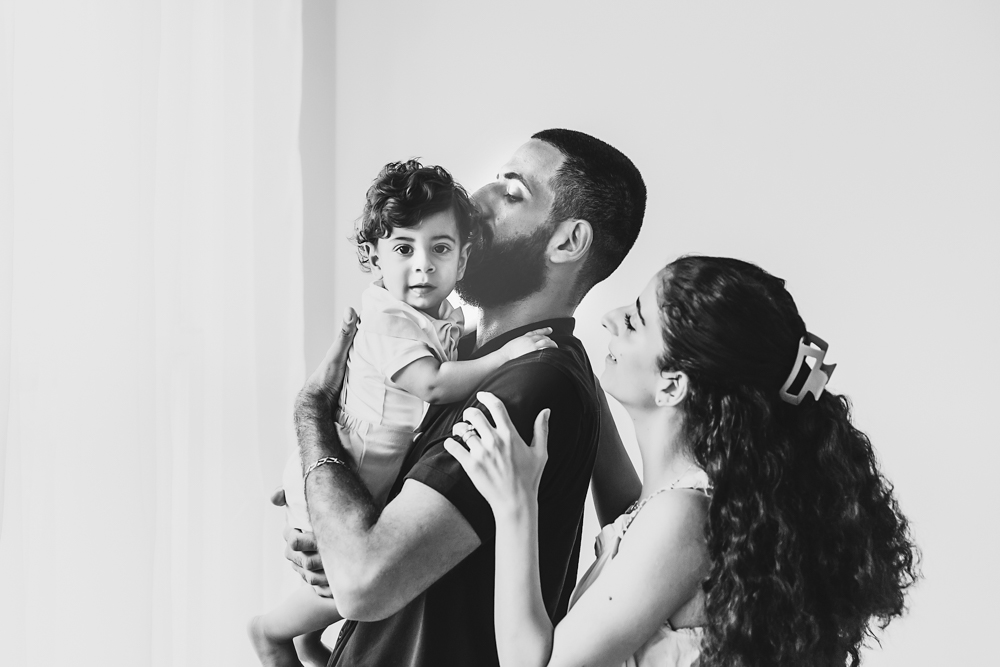 Black and white portrait of dad holding Lucas while mom stands close in soft window light at Reflection Images by Tracy Rowell in Florence SC