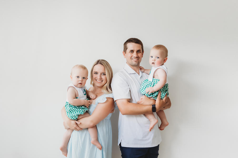 Family portrait of parents holding twins in front of a white wall at Reflection Images by Tracy Rowell in Florence SC