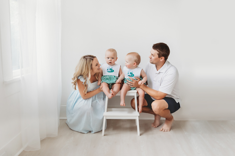 Parents kneeling with twins beside a window in bright natural light at Reflection Images by Tracy Rowell in Florence SC