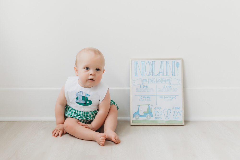Nolan sitting on a light wood floor beside his blue birthday milestone board at Reflection Images by Tracy Rowell in Florence SC