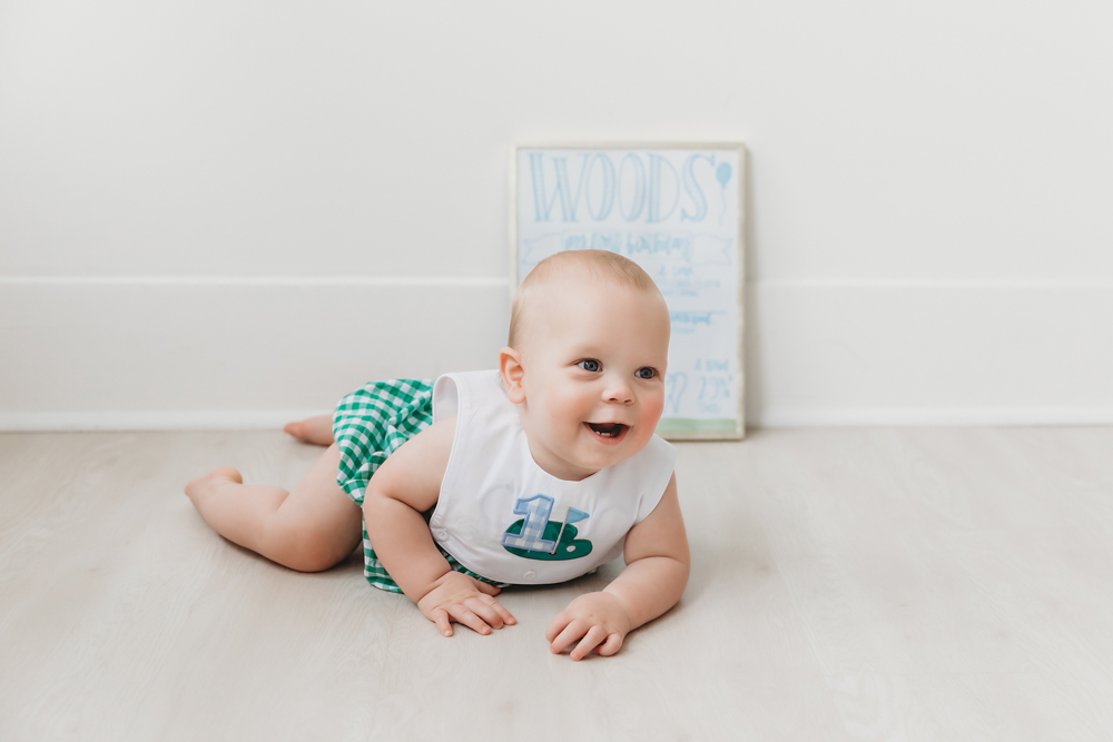 Woods smiling while lying on his tummy near his birthday milestone sign at Reflection Images by Tracy Rowell in Florence SC