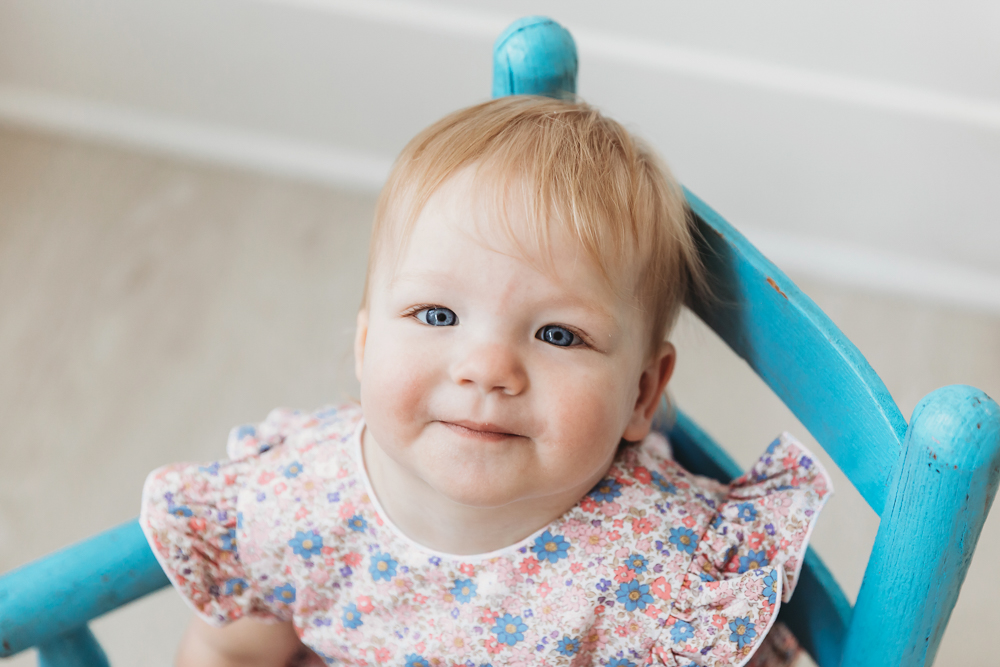 Top-down view of Hadley looking up with soft eyes, seated in a vintage blue wooden chair at the studio