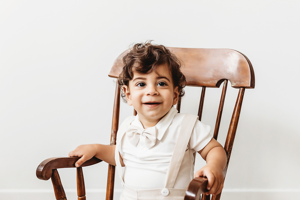 Closeup of Lucas smiling while sitting in a wooden rocking chair against a clean white backdrop at Reflection Images by Tracy Rowell in Florence SC