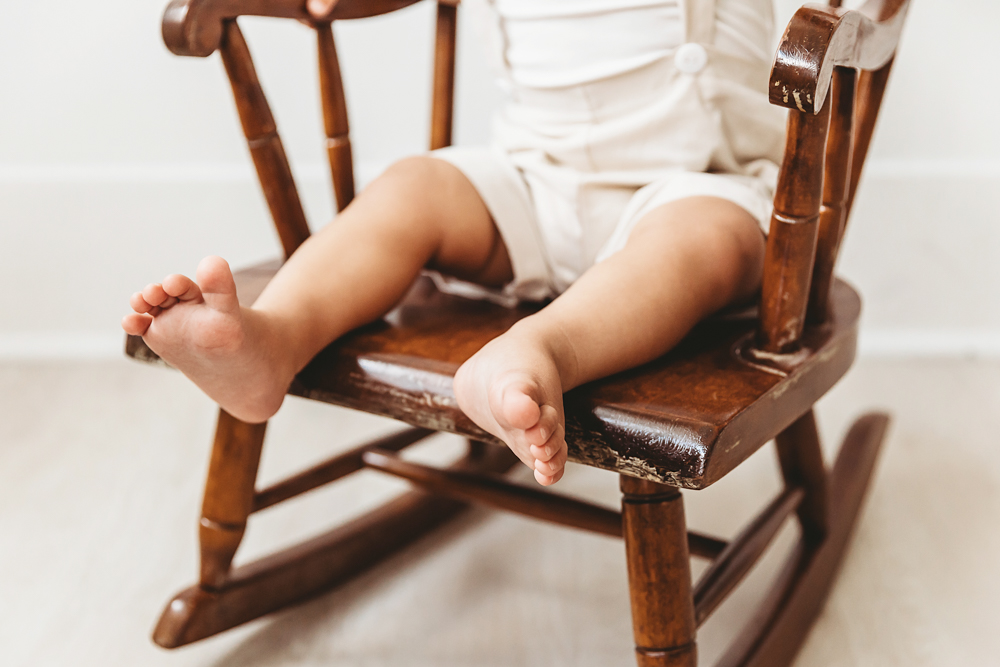 Close detail of Lucass small feet resting on a wooden rocking chair seat in bright studio lighting at Reflection Images by Tracy Rowell in Florence SC