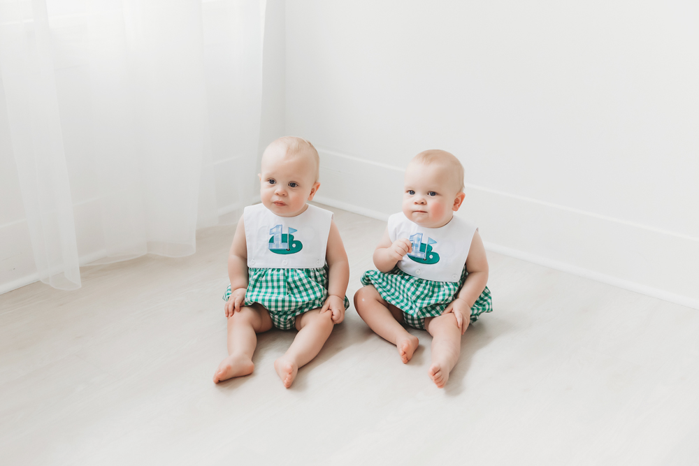 Twins sitting side-by-side in front of white wall with light flooding in at Reflection Images by Tracy Rowell in Florence SC