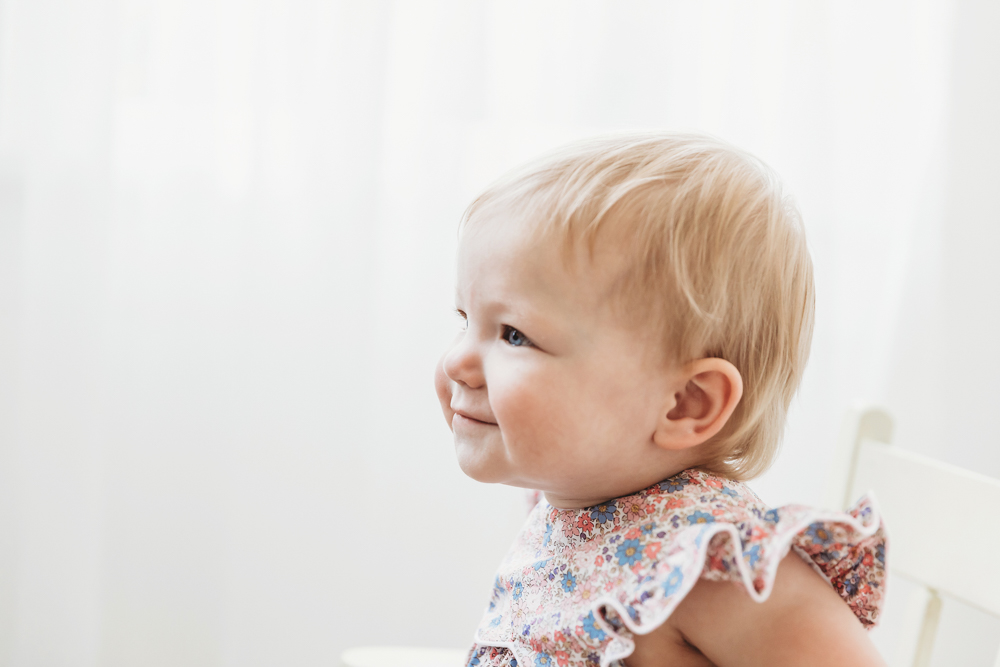 Side profile of Hadley smiling softly in floral romper with gentle window light from the right