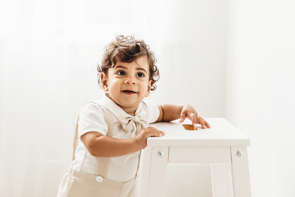 Lucas stands holding a white step stool while smiling softly toward the camera in bright natural light at Reflection Images by Tracy Rowell in Florence SC