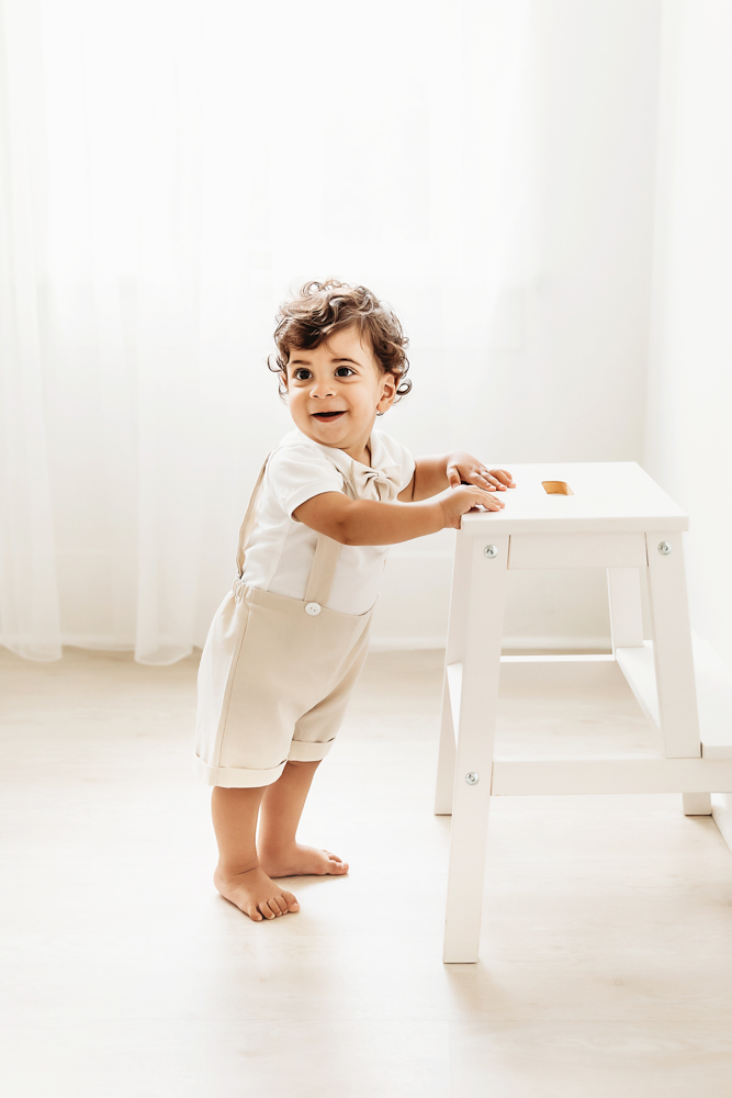 Full body portrait of Lucas standing barefoot at a white stool in airy window light at Reflection Images by Tracy Rowell in Florence SC