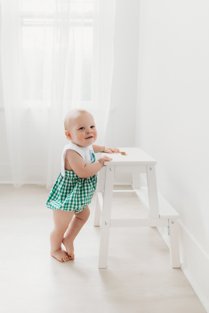 One twin standing at a white step stool, smiling near window at Reflection Images by Tracy Rowell in Florence SC
