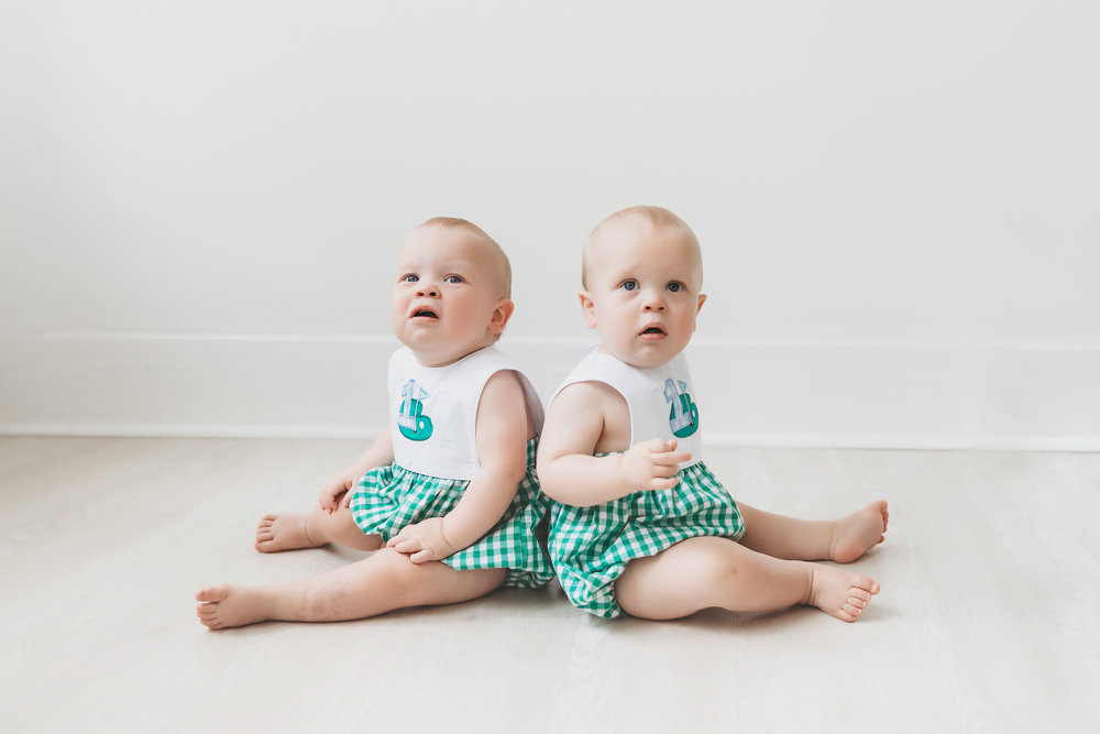 Back-to-back portrait of twins sitting in matching outfits on the studio floor at Reflection Images by Tracy Rowell in Florence SC