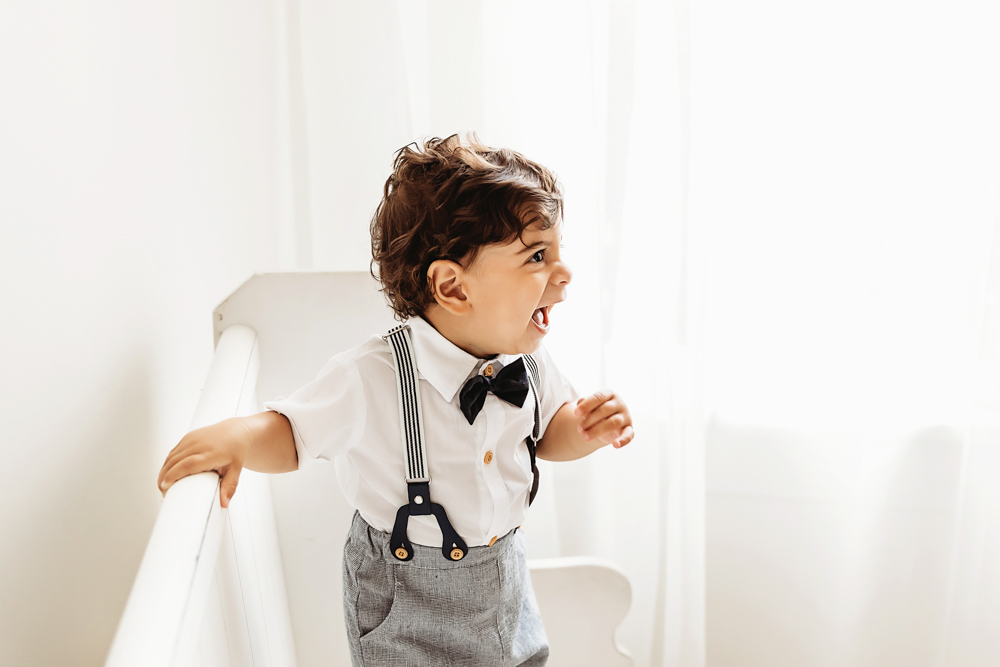 Side view of Lucas laughing excitedly while holding a crib rail in soft curtain filtered studio light at Reflection Images by Tracy Rowell in Florence SC