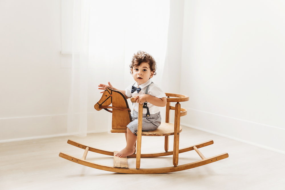 Lucas sits facing forward on a wooden rocking horse looking toward the camera in bright window light at Reflection Images by Tracy Rowell in Florence SC
