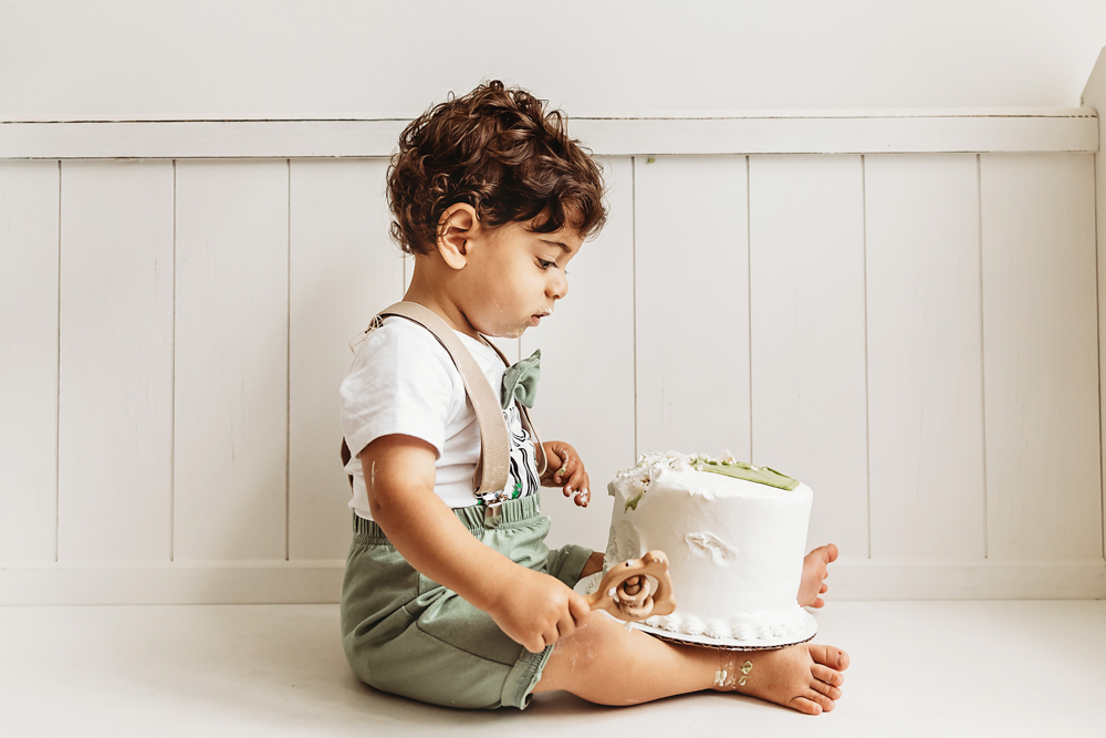 Side view of Lucas sitting cross legged in green suspenders inspecting his cake during a smash session at Reflection Images by Tracy Rowell in Florence SC