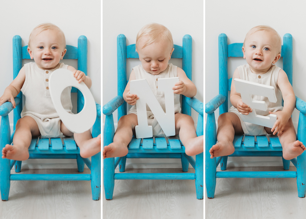 Baby in cream romper on turquoise chair holding white ONE letters for first birthday - Reflection Images by Tracy Rowell