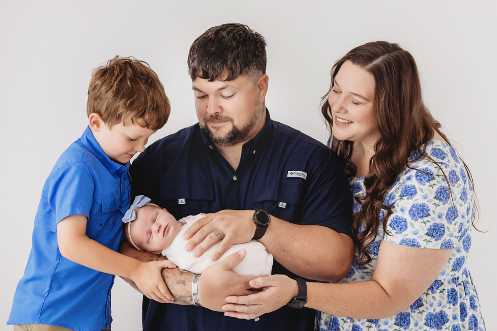Family of four with newborn baby on white backdrop - professional photography near me in soft studio lighting