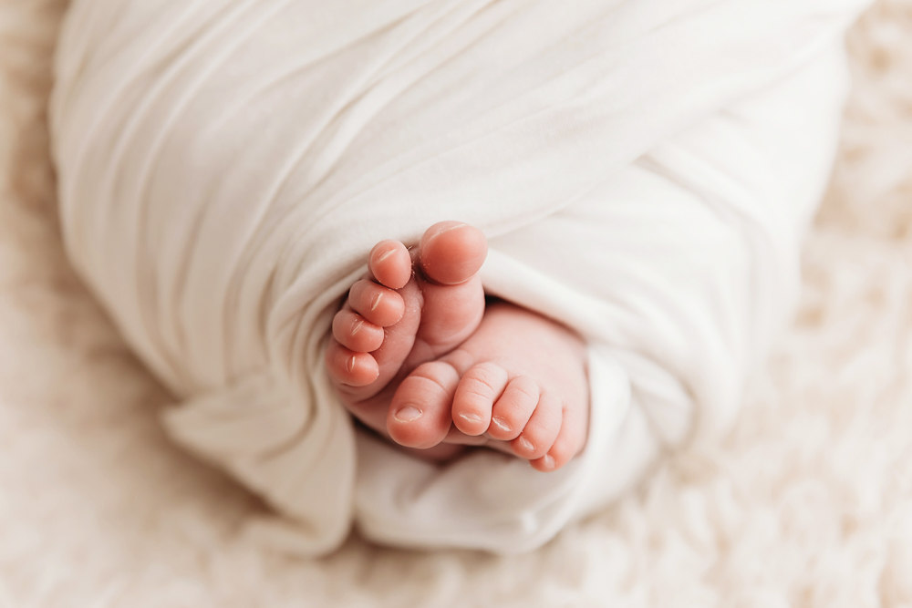Newborn baby feet peeking through cream knit blanket, soft natural lighting, intimate portrait by Tracy Rowell