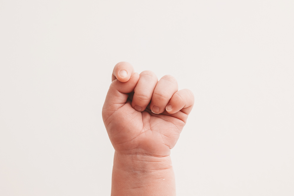Tiny baby fist raised against soft cream backdrop, professional photography near me capturing delicate newborn details
