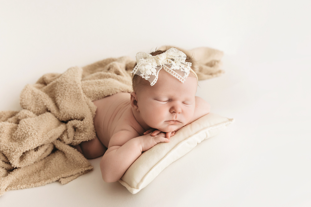 Sleeping newborn baby with cream lace headband on beige blanket, soft studio lighting - Reflection Images by Tracy Rowell