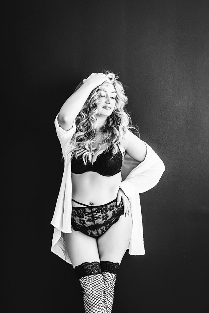 Adult woman in black lingerie and white blazer poses confidently celebrating womanhood in dramatic B&W studio portrait