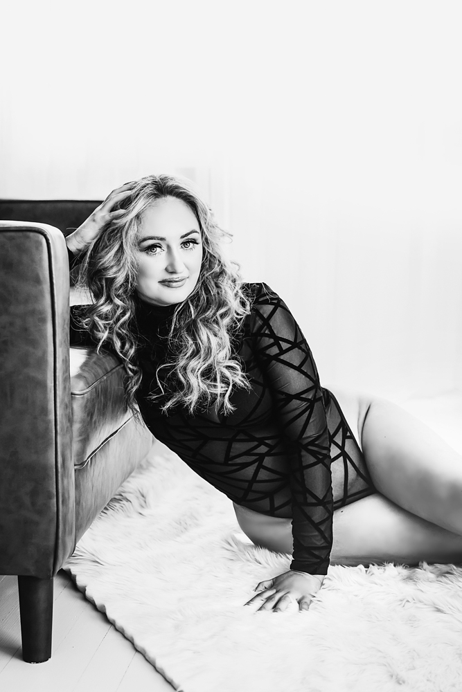 Adult woman in black lace outfit posing on cream chair, curly blonde hair, soft studio lighting - see yourself in portraits