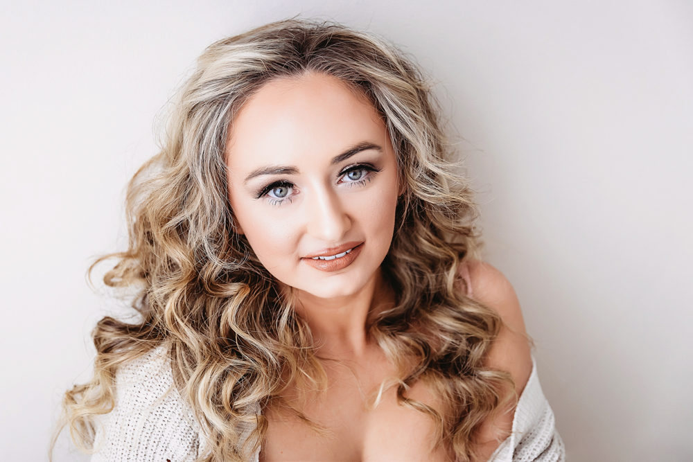 Woman with blonde curly hair in white knit sweater smiling at camera, soft lighting portrait by south carolina boudoir photographer
