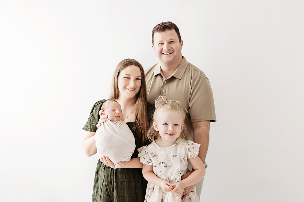 Family portrait: parents with newborn and young daughter on white backdrop, professional photography studio near me