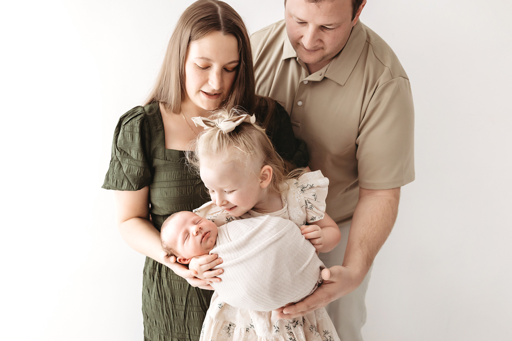 Family of four with newborn baby in cream studio setting by professional photographer near me, soft natural lighting