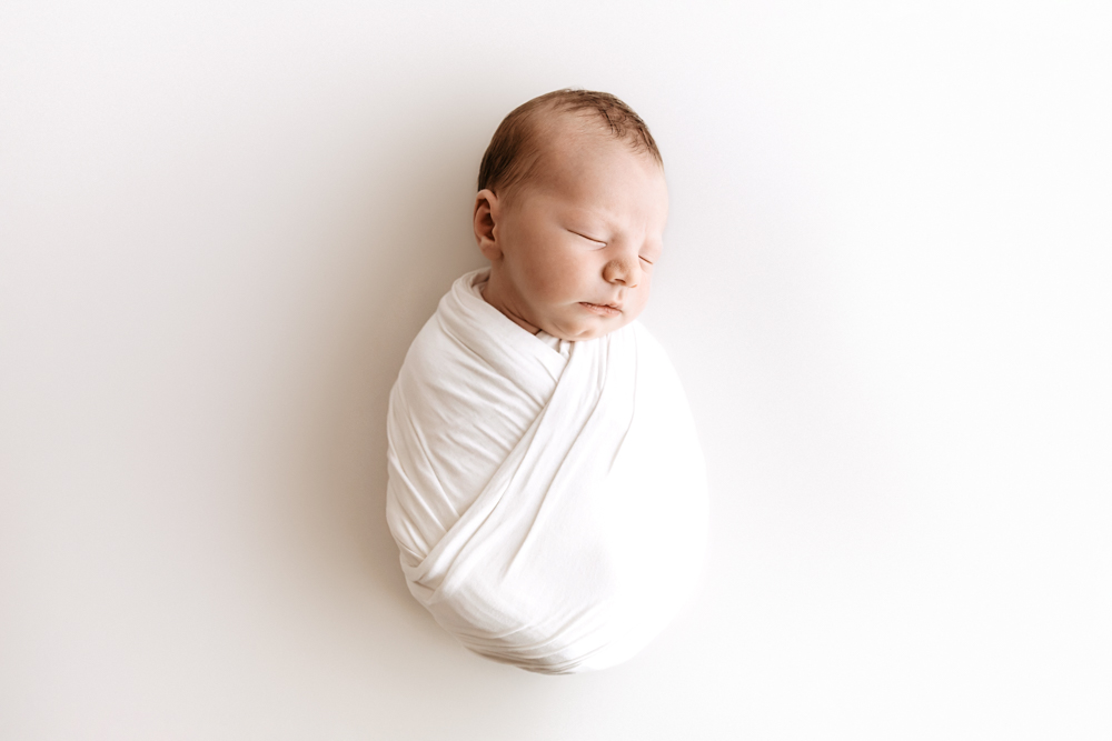 Peaceful sleeping newborn baby wrapped in white swaddle on cream backdrop by florence sc photographer