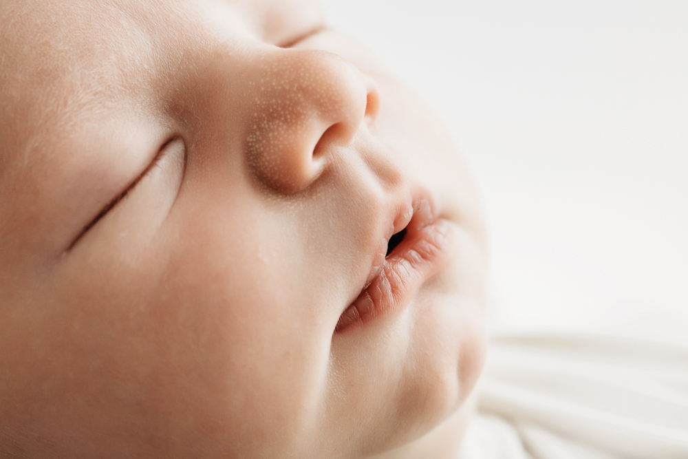 Peaceful baby sleeping with hand near face on white backdrop, soft natural lighting, professional photographer near me