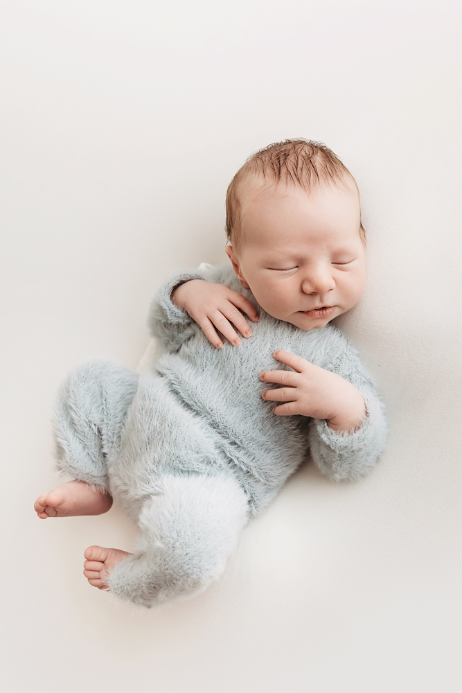 Sleeping newborn baby in soft gray knit romper on cream backdrop, peaceful newborn photos with gentle studio lighting