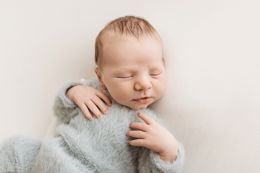 Sleeping newborn wrapped in soft gray knit blanket on cream backdrop for newborn pictures, peaceful studio portrait