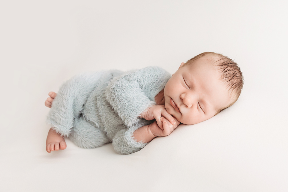 Sleeping newborn in soft blue knit wrap on cream backdrop by florence sc newborn photographer