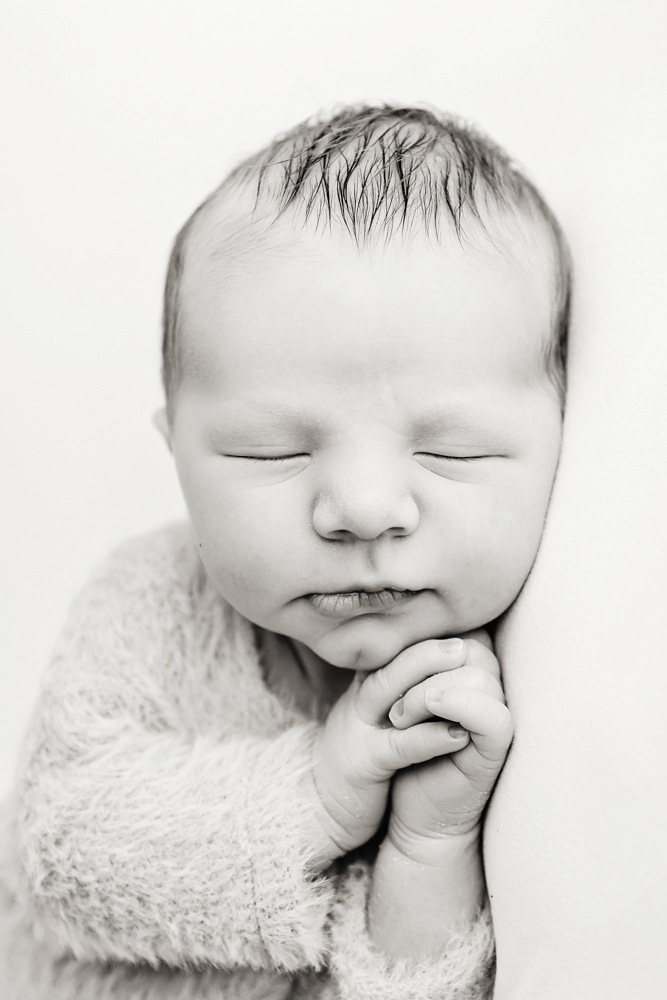 Peaceful sleeping newborn baby in soft textured blanket, hands clasped, black and white professional photography studio near me