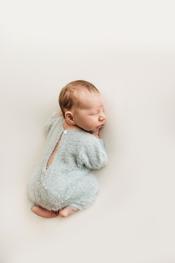 Sleeping newborn baby wrapped in soft sage green blanket on cream backdrop, professional photography near me